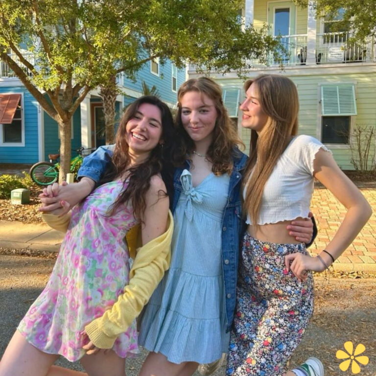 Three friends in bright outfits pose playfully in a sunny street.