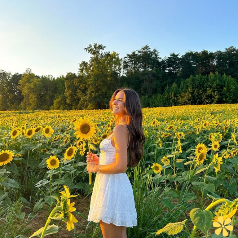 Woman in white dress smiling in sunflower field at sunset