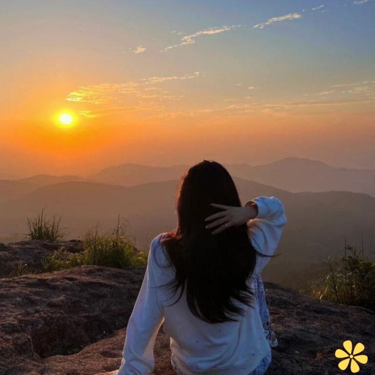 A woman gazes at a stunning sunset over rolling hills, her hair flowing gently in the breeze.