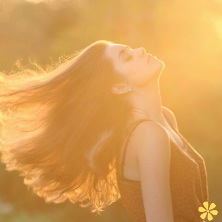 A woman with flowing hair stands against a bright golden light, her face serene and eyes closed.