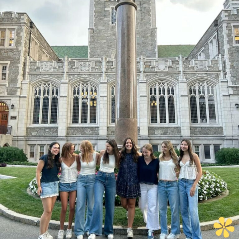 Group of friends smiling and posing by a tall pillar in front of a historic building.