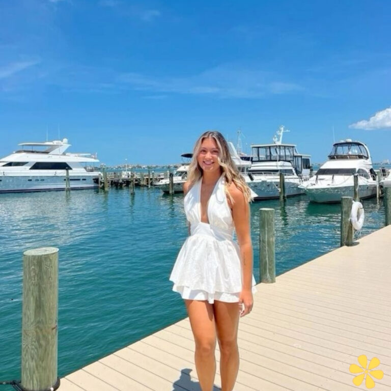 Smiling young woman in a white dress standing on a dock by boats.