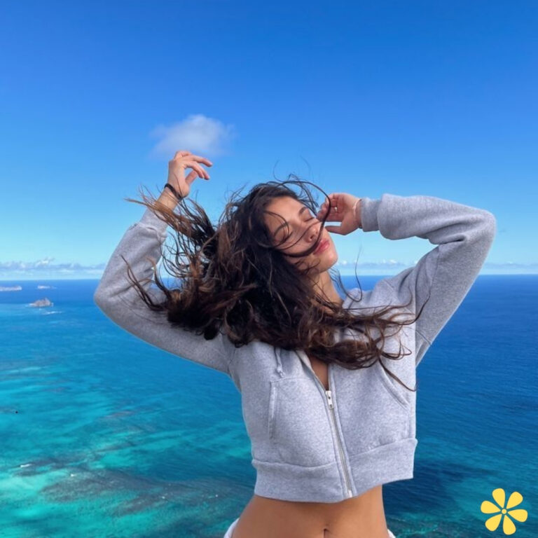 Young woman with long hair joyfully poses against a stunning ocean view.