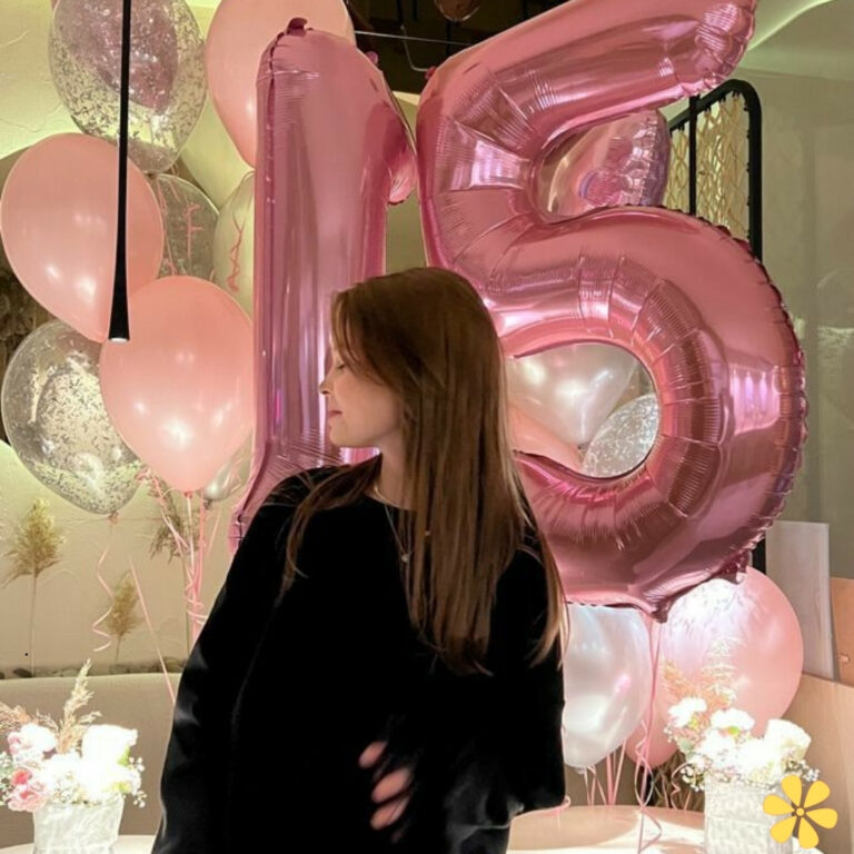 A young woman turns slightly, with pink balloons and a '15' decoration behind her.