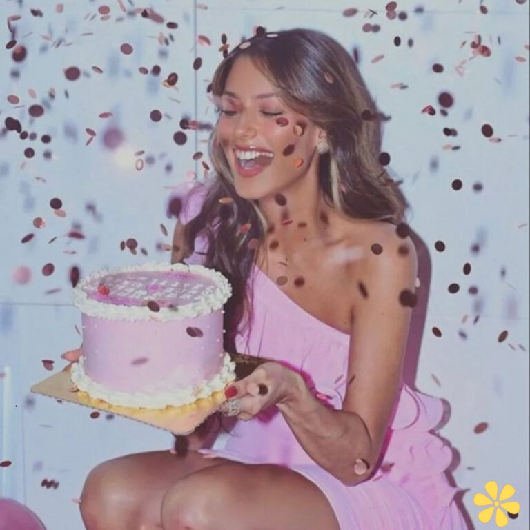 Woman in a pink dress joyfully holding a cake amidst confetti.