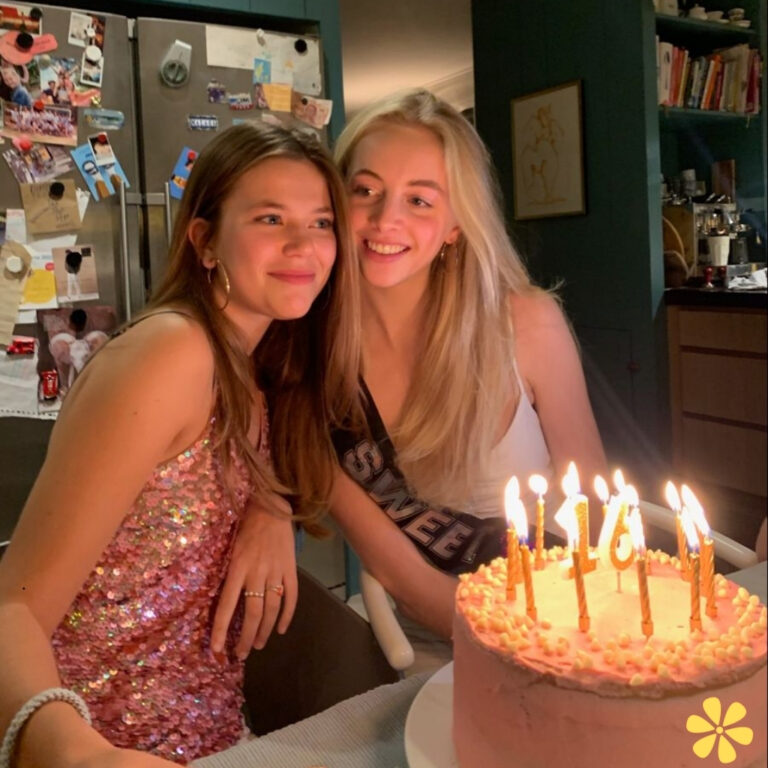 Two friends share a joyful moment by a birthday cake, surrounded by warm light.