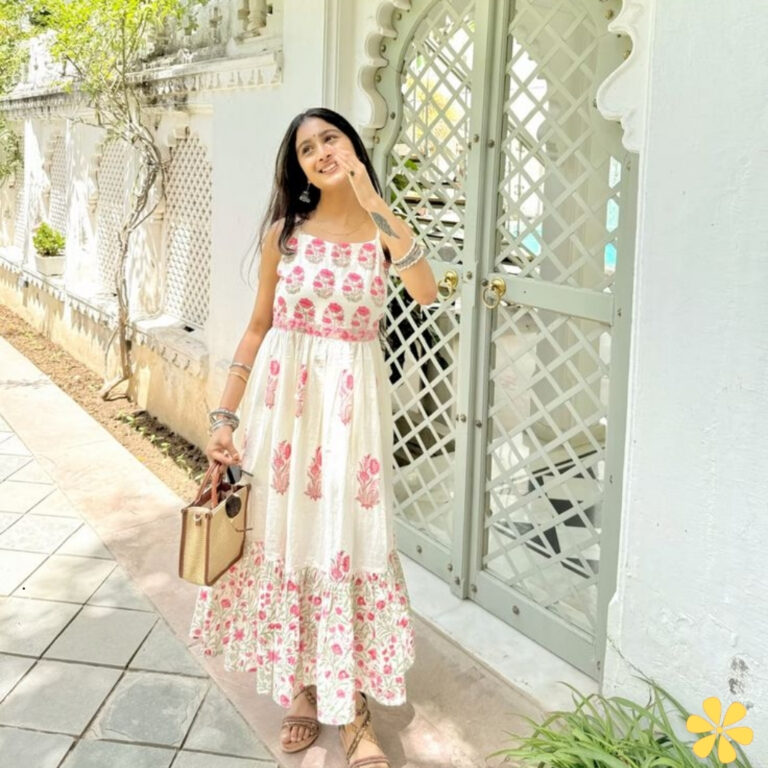 Smiling woman in floral dress poses by a decorative gate.