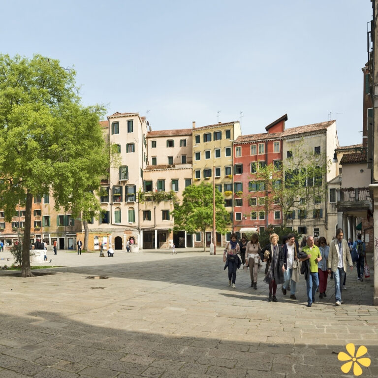 People walking through a vibrant plaza with colorful buildings and trees.