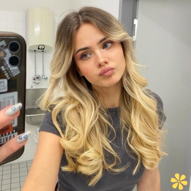 Woman with long, wavy hair poses in front of a mirror, wearing a casual black top.