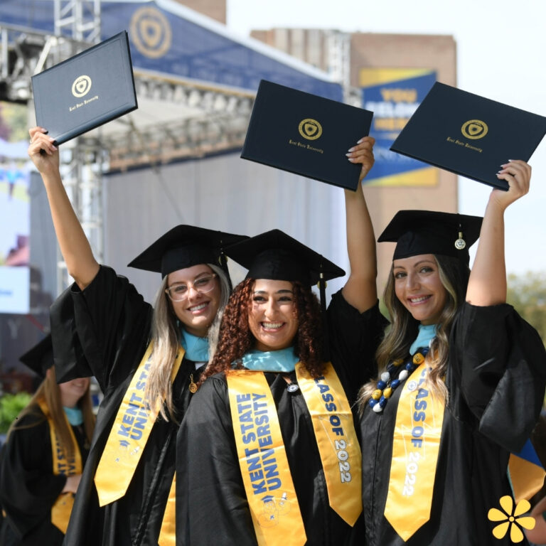 Three graduates joyfully holding their diplomas in caps and gowns.