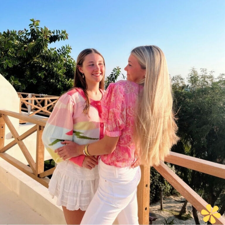 Two friends smiling on a balcony in colorful outfits.