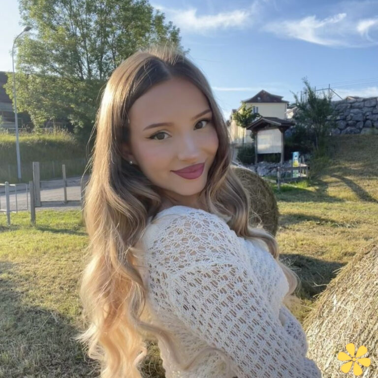 Smiling woman with long hair in a cozy sweater, posing outdoors near hay bales.