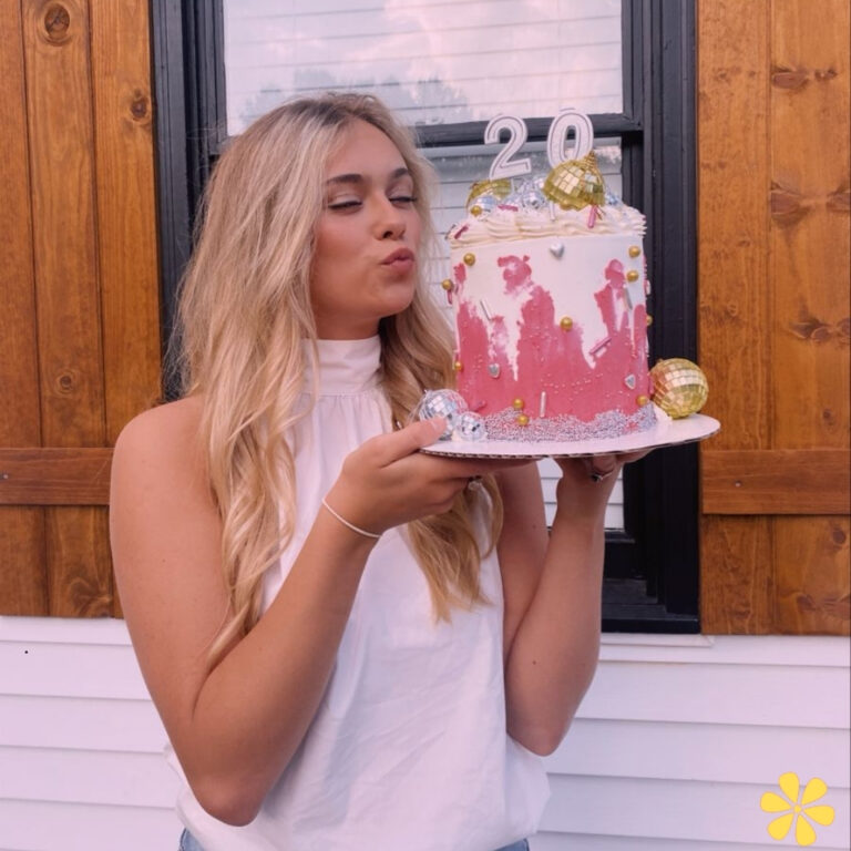 Woman with long hair holds a pink birthday cake, blowing a kiss, celebrating her 20th birthday.