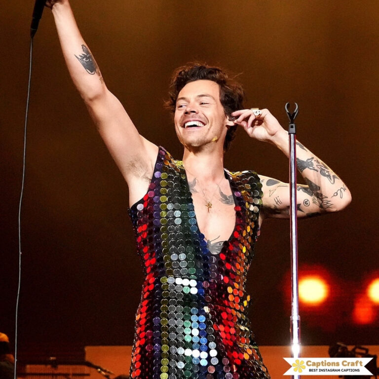 Singer in a sparkly vest raises hand, smiling brightly.